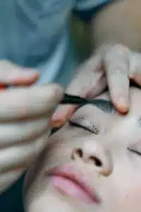 Immagine di una donna che oltre ad avere il volto segnato dai tratteggi pre operazione al volto ha intornp le mani dei chirurghi con forbici e attrezzi vari